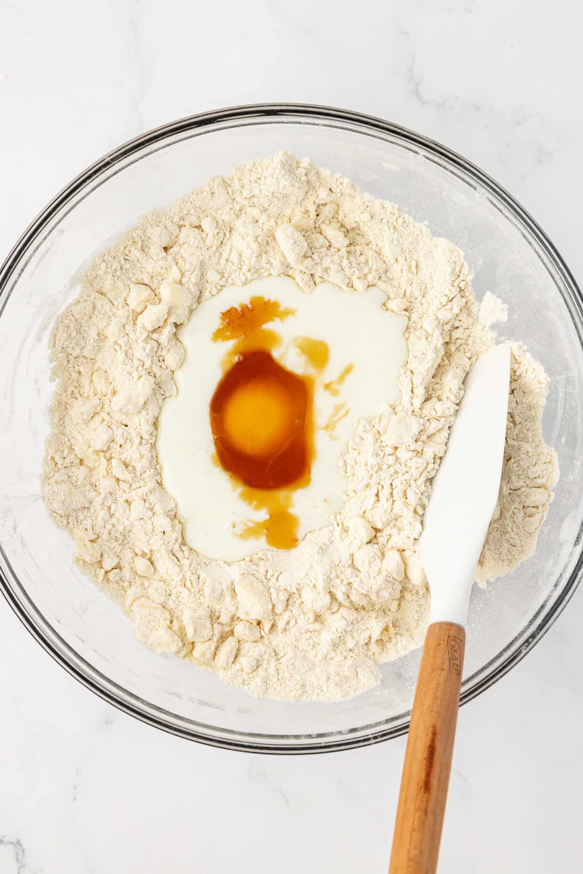 flour, buttermilk, egg and other wet ingredients for shortcake biscuits in a clear glass bowl with a white spatula